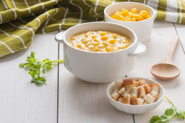 Corn soup in white bowl and crispy bread with corn on white table.