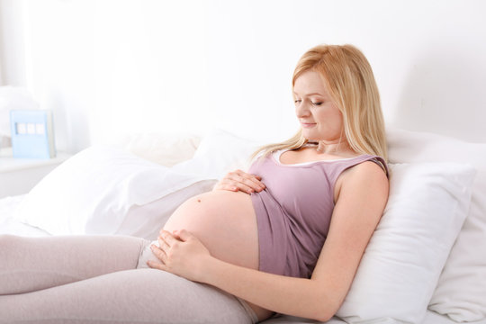 Beautiful pregnant woman resting on bed in light room