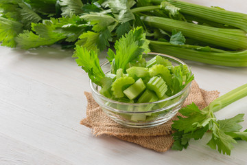 Fresh celery sliced in bowl with bunch celery on white wood background.