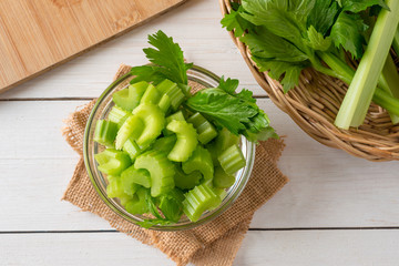 Fresh celery sliced in bowl with bunch celery on white wood background. Top view.