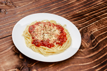 close in meal of noodles with red sauce and grated cheese on white plate, wooden background