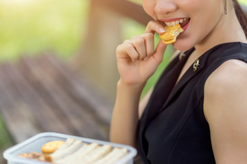 Woman eating healthy peanut butter sandwich cracker sitting at park, appetizer lunch box.
