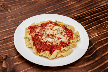 close in penne meal with red sauce and grated cheese, wooden background