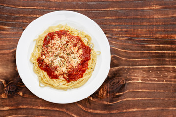 meal of noodles with red sauce and grated cheese on white plate, wooden background, top view
