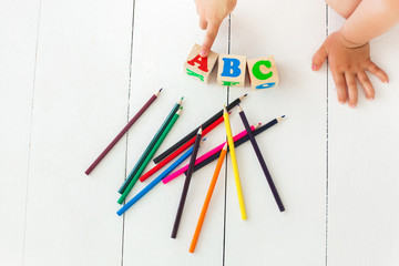 Little child pointing the abc cubes. Alphabet background. abc bricks on the neutral background. colorful pencils