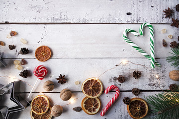 Christmas or New Year decoration, fir tree, tangerine, candy cane, dry oranges, sugar, wallnuts and cookie cutters on white wooden background