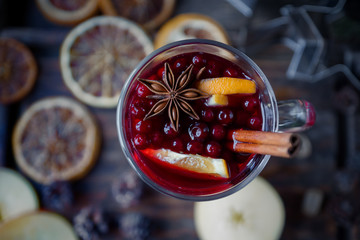 Homemade mulled wine with oranges, apples, cinnamon, cranberries and fir tree on rustic wooden...