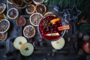 Homemade mulled wine with oranges, apples, cinnamon, cranberries and fir tree on rustic wooden background