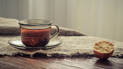 tea in a transparent glass cup and dried lemon on the edge of a rough burlap tablecloth on old boards in natural light