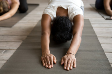 Black yogi woman and group of young sporty people practicing yoga lesson, doing Child exercise,...