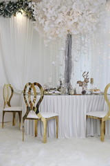 Dinner table with golden chairs with white new Year and wedding decor 