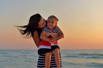 Young mother with a little daughter playing on the beach at sunset.