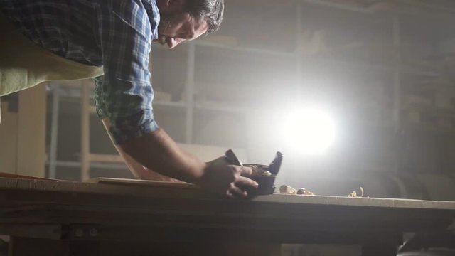 portrait male carpenter in shirt in dark workshop planing wood
