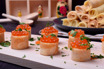 Crepes with red caviar on a wooden board sprinkled with parsley. Russian cuisine