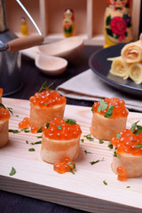 Crepes with red caviar on a wooden board sprinkled with parsley. Russian cuisine