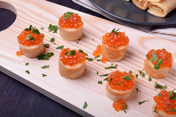 Crepes with red caviar on a wooden board sprinkled with parsley. Russian cuisine