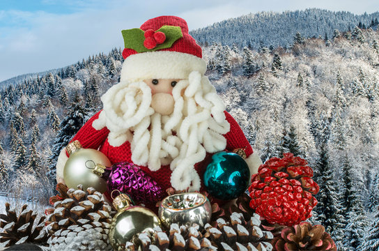 Toy Santa Claus with Christmas decorations against the backdrop of a winter landscape with mountains covered with forests.