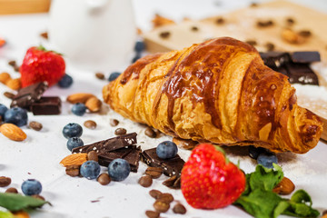 Breakfast includes croissants, fresh blueberries and chocolate on the wooden table.