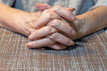 The hands of an elderly woman resting on the table. Parkinson.