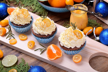 Cupcakes topped with butter cream, slices of kumquat and rosemary surrounded by fruits. Christmas dessert