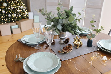 Elegant Christmas tree with gifts in the living room with dinner table near the textured gray walls in luxury apartments. 