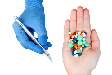 Hands holding pills capsules tablets and scalpel with blue rubber glove isolated on white. Concept...