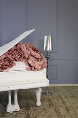 white grand piano decorated with pink pale yellow peonies made of paper in luxury suites with gray walls and a silver lamp