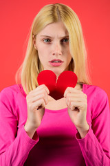 Sad woman tearing paper heart to pieces. Attractive blonde girl holds broken paper red valentine heart. Broken hearted on Valentines day. Concept of unrequited love. Girl with red paper heartbreak.