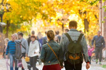 Young couple in love walking in the middle of the crowd in the autumn sunny park