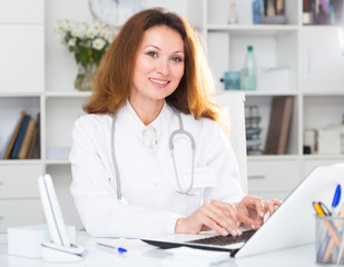 Portrait of female doctor who is working with laptop and documents