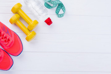 Fitness equipment with copy space. Sport shoes, dumbbells, bottle of water and measuring tape on white wooden background.