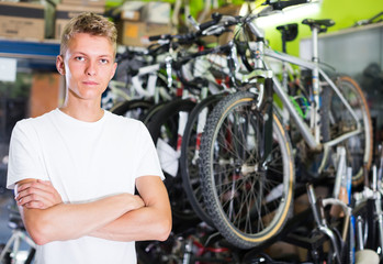 Obraz na płótnie Canvas young serious male standing near the cycle in the shop