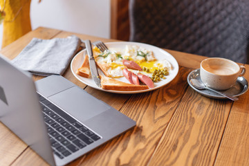 The concept of eating at work. Laptop and Breakfast on the table.. American style breakfast with fried eggs, sausage, green peas and toast. The concept of a healthy morning.