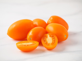 Orange tomatoes on white marble table. Yellow or orange tomatoes heap with two half sliced tomato. Copy space for text