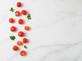 Naklejka na ściany i meble Orange tomatoes on white marble table. Small red cherry tomatoes with half sliced tomato and fresh parsley leaves. Top view or flat lay. Copy space for text.