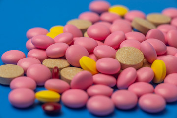 Multicolored medical tablets, pills, vitamins, close up on blue background