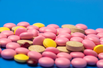 Multicolored medical tablets, pills, vitamins, close up on blue background