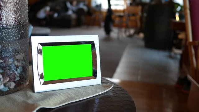 A green screen picture frame sitting on an end table with blurry people in background