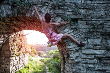 The girl climbs the stone wall.