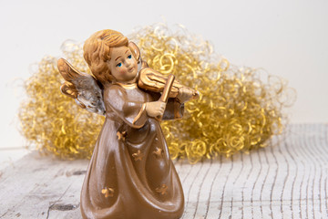 Angel with violin in front of golden hair on white wood as Christmas background