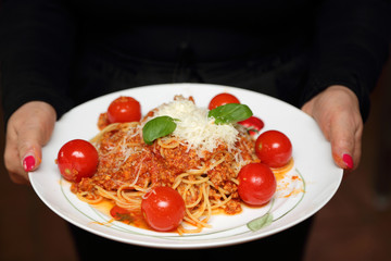 Dłonie kobiety trzymają talerz spaghetti i pomidorami. - obrazy, fototapety, plakaty