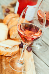 Two glasses of rose wine and board with fruits, bread and cheese on wooden table