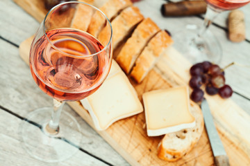 Two glasses of rose wine and board with fruits, bread and cheese on wooden table - 235366682