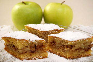 Three pieces of homemade traditional apple cake with two organic green apples in a background