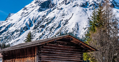 Wood cabin with snowy mountains in the distance and pine trees, taken in Lech, Austria