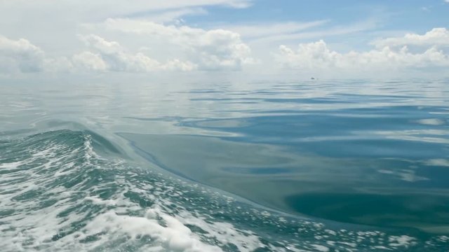 Small foamy blue waves after a boat and calm ocean in cloudy day. Idyllic tropical waterscape. The sky is reflected in the surface of the quite water of the sea. windless weather