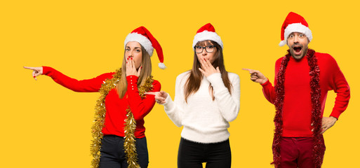 A group of people Blonde woman dressed up for christmas holidays pointing finger to the side with a surprised face on yellow background