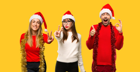 Fototapeta premium A group of people Blonde woman dressed up for christmas holidays smiling and showing victory sign on yellow background