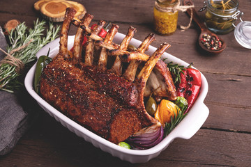 Grilled roasted rack of veal lamb chops with vegetables in ceramic baking dish.