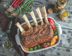 Grilled roasted rack of veal lamb chops with vegetables in ceramic baking dish.